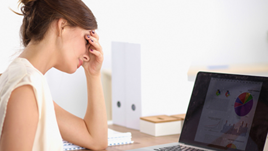 Woman holding her head in pain while working on laptop