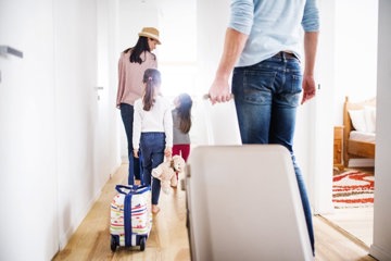 Familie, welche die Wohnung mit Koffern verlässt und in den Sommerurlaub aufbricht 