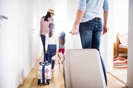 Familie, welche die Wohnung mit Koffern verlässt und in den Sommerurlaub aufbricht