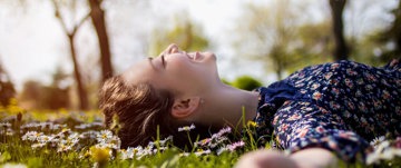 A woman reclines peacefully in a vibrant field of daisies, surrounded by nature's beauty and tranquility.