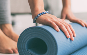 Eine Person greift eine Yogamatte, um sich auf eine bevorstehende Yoga-Praxis vorzubereiten.