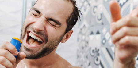 Ein Mann unter der Dusche, der eine Duschgelflasche in der Hand hält. Er singt und verwendet die Duschgelflasche als Mikrofon.